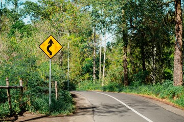 Winding road with yellow sign for a sharp curve through a forest. Traffic sign on mountain route.