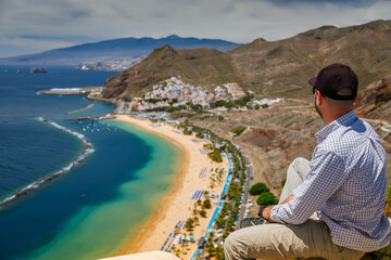 Scenic view from above of Las Teresitas beach in Tenerife, where a tourist man sits, enjoying the picturesque landscape