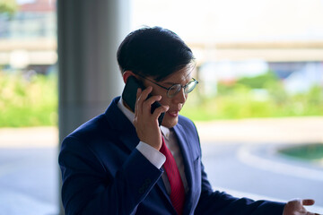 Asian businessman wear formal blue navy suit talking with phone for communicate business out of office.