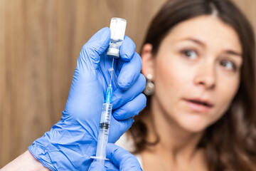 Gloved hand holding a syringe and vial for injection with blurred patient face in background