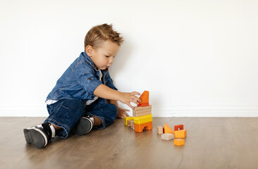 A boy carefully stacks brightly colored blocks, concentrating intently as he constructs a structure. The setting is simple and well-lit, emphasizing his focused playtime.