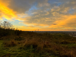 Sunset over fields and trees in a green hilly landscape under a colorful sky