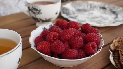 Plate of raspberry on the wooden table surrounded by tea cups and plates.