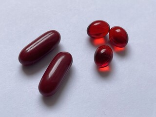 A close-up image of red gelatin capsules, showcasing two larger pills and three smaller ones against a plain background.
