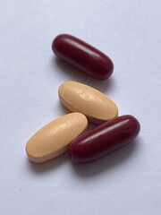 A close-up image showing two red and two beige oval pills arranged on a white surface, illustrating pharmaceutical products.
