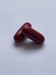 Two red capsules resting on a white surface, showcasing their smooth texture and sleek design.
