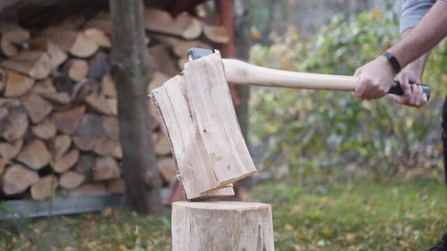 Splitting logs with an axe in slow motion, chips flying in the air. Firewood is stacked in the background, with a sunny day brightening the scene.