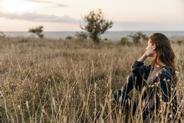 Peaceful woman sitting in a sunlit field gazing at the vast expanse of the ocean