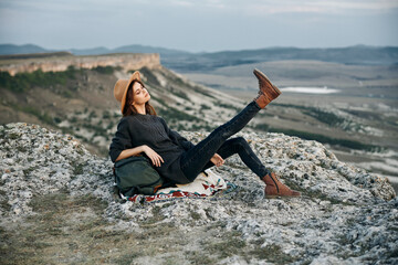 Serene woman sitting crosslegged on rock with backpack nearby in peaceful nature setting
