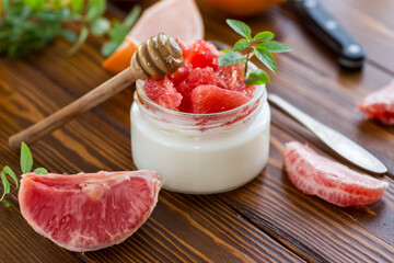 homemade sweet yogurt in a glass jar with pieces of red ripe grapefruit and honey, on a wooden table