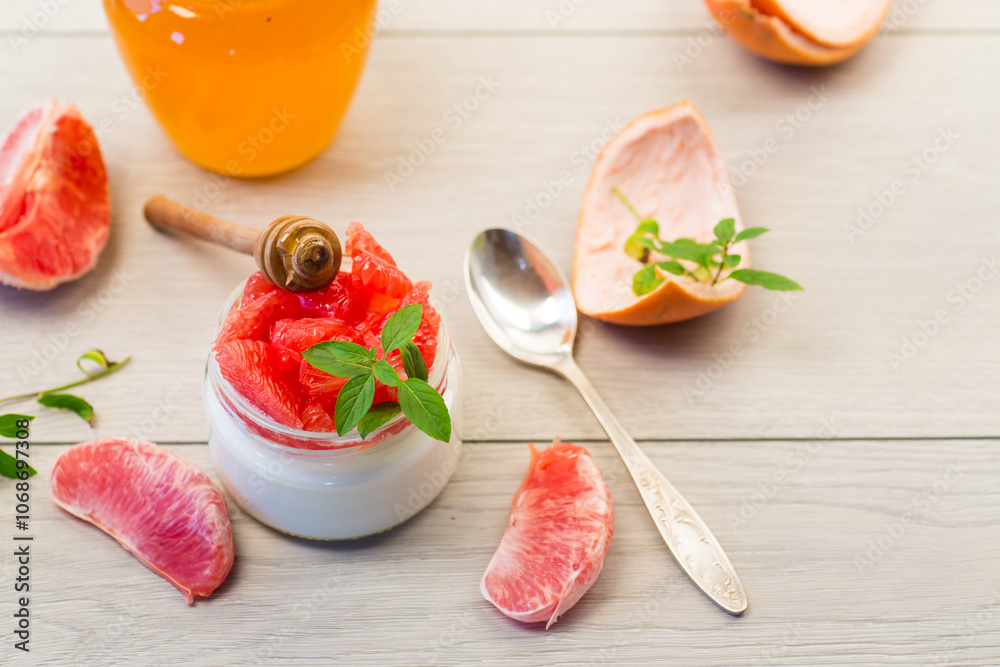 Wall mural homemade sweet yogurt in a glass jar with pieces of red ripe grapefruit and honey, on a wooden table