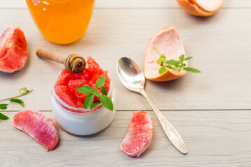 homemade sweet yogurt in a glass jar with pieces of red ripe grapefruit and honey, on a wooden table