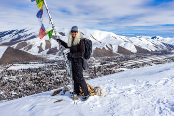 Smiling woman with snowshoes standing at pole with colorful flags on top of mountain
