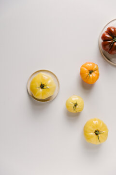 Different colored and sized tomatoes on a light table top.