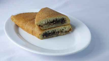 A plate holding two slices of rolled pancake, showing a golden-brown. The slices are filled with a dark mixture are positioned on a clean white plate against a light backdrop