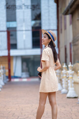 Fototapeta premium A woman wearing a straw hat and a yellow dress is walking down a street