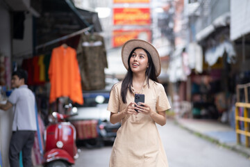 Fototapeta premium A woman wearing a hat and holding a cell phone walks down a street