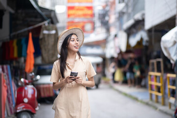 A woman wearing a hat and holding a cell phone walks down a street