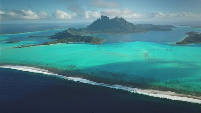Breathtaking aerial view of Bora Bora's main island with turquoise lagoon, vibrant coral reefs and lush greenery under blue sky. Remote wild nature paradise, exotic summer travel. Drone panorama