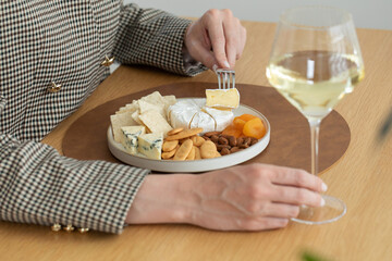 A glass of white wine in your hand against the background of a cheese plate with snacks and nuts