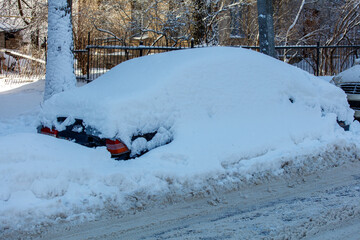 A car is covered in snow and is parked on a snowy street