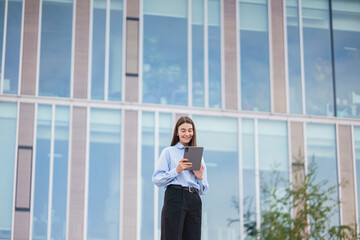 Young Woman Using a Tablet Outdoors at a Modern Office Building on a Sunny Day in an Urban Setting