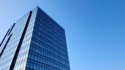 Modern office building with sleek glass facade standing tall against a clear blue sky backdrop, clear sky