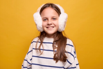Friendly delighted small child in fur headphones with heartwarming smile looking pleased and...