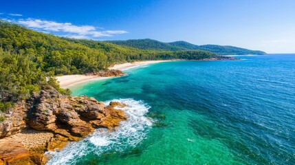 Scenic beach with crystal clear water, golden sands, and lush green hills under a blue sky.