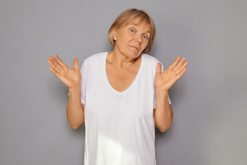 Senior uncertain upset woman hunched over unsure of answer feeling confused and uninterested denying question with disinterest isolated over gray background