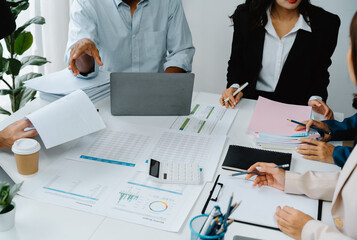 Strategic Business Meeting: A high-angle, close-up shot captures a diverse team of professionals engrossed in a collaborative meeting, surrounded by financial documents, laptops.