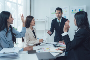 Business Meeting Brainstorming: A team of four professional business people engaged in a lively brainstorming session, with one person raising their hand to contribute an idea.