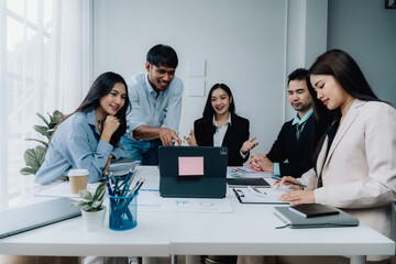 Fototapeta premium Collaborative Brainstorming: A diverse team of professionals engage in a lively discussion around a laptop, showcasing the dynamic and collaborative nature of modern business. 