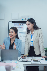 Businesswomen Collaboration: Two diverse professional women engage in a productive discussion, leaning over a laptop and documents, symbolizing collaboration, innovation.