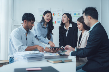 Fototapeta premium Business Team Collaboration: A diverse group of business professionals collaborate during a productive meeting, engaging in a lively discussion around a tablet, showcasing teamwork and communication.