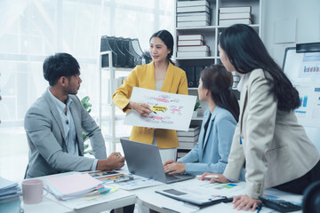 Business Meeting: A diverse team of professionals collaborates in a modern office setting. The woman in the center presents a colorful diagram to her colleagues.