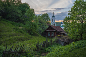 Beautiful spring landscape overlooking an old wooden house. In the background is a view of the bell tower and domes of the Varvarinskaya Church, amazing sunset in the city of Ples.