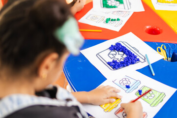 Girl learning about recycling with a school assignment where she colors trash containers, early learning about environmental care, coloring