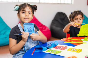 A Latina elementary school girl proudly shows a cutout from her recycling project, with visible...