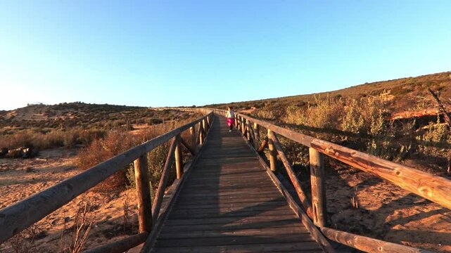 Mature woman on a walkway with wooden steps on Cuesta Maneli beach, located in a very unique environment, the fossil dune system of El Asperillo, located within the Do&ntilde;ana Natural Park, Huelva, Spain.
