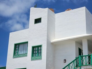 Ce bâtiment blanc typique de Costa Teguise arbore des fenêtres encadrées de vert, reflétant le style architectural des Canaries sous un ciel bleu éclatant.