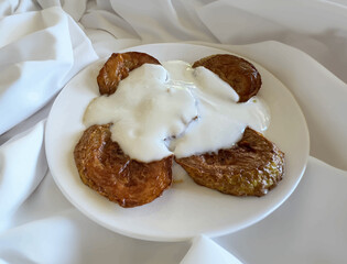 Illustration of fried zucchini with yogurt. Fried round zucchini slices isolated in a white plate. Fried zucchini slices on a plate with yogurt on top. Unhealthy food. Fatty food, obesity.