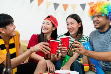 Fototapeta premium A group of excited Asian male and female friends watched the World Cup match on TV and drank beers and ate snacks together at home. Sports fans shout and celebrate the victory of their sports team.