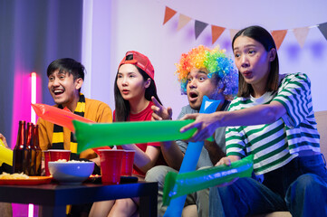 A group of excited Asian male and female friends watched the World Cup match on TV and drank beers and ate snacks together at home. Sports fans shout and celebrate the victory of their sports team.