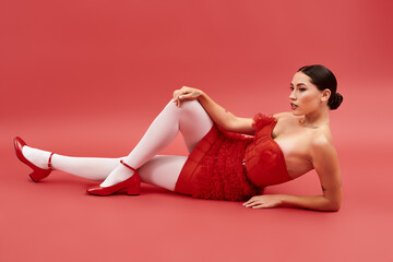 Dressed in a radiant red outfit, a graceful woman poses artistically, exuding confidence and charm.