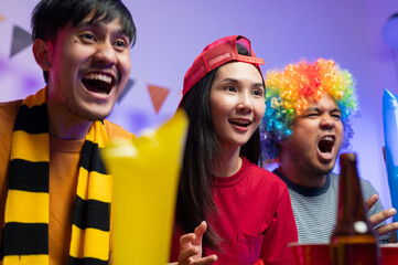 A group of excited Asian male and female friends watched the World Cup match on TV and drank beers and ate snacks together at home. Sports fans shout and celebrate the victory of their sports team.