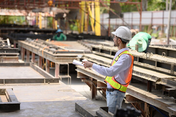 Young engineer wearing a hard hat in a factory inspecting the work on a construction site and pouring cement.