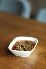 A close-up of a traditional Turkish appetizer, közlenmiş biber salçası, served in a white bowl on a wooden table