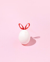 Easter egg with ribbon bunny ears, creative concept, pastel pink background.