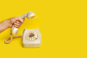 Man hand holding a vintage telephone handset on a yellow background with copy space